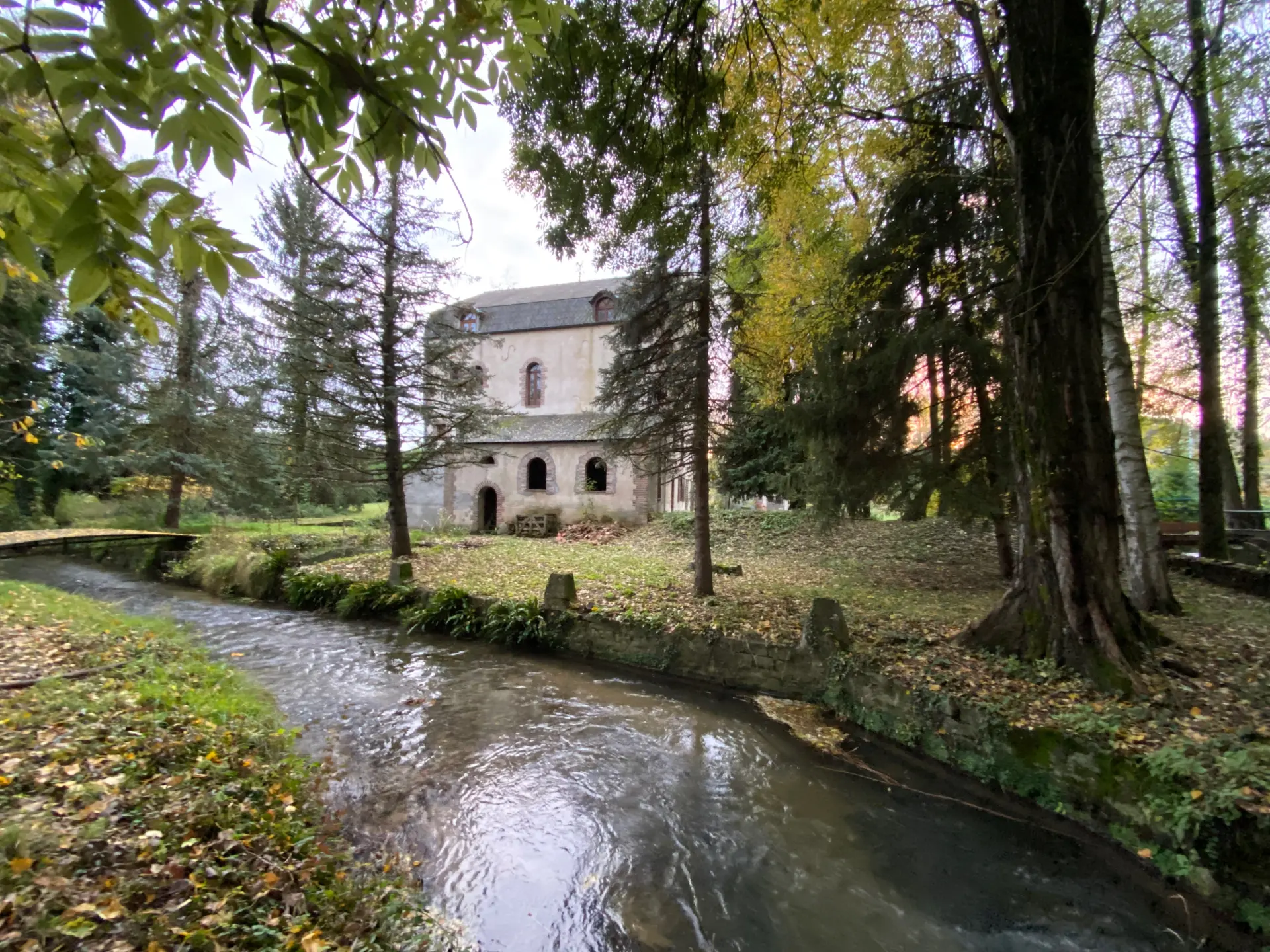 Le Moulin d’en Bas vu depuis le bief, entre les arbres d’automne.