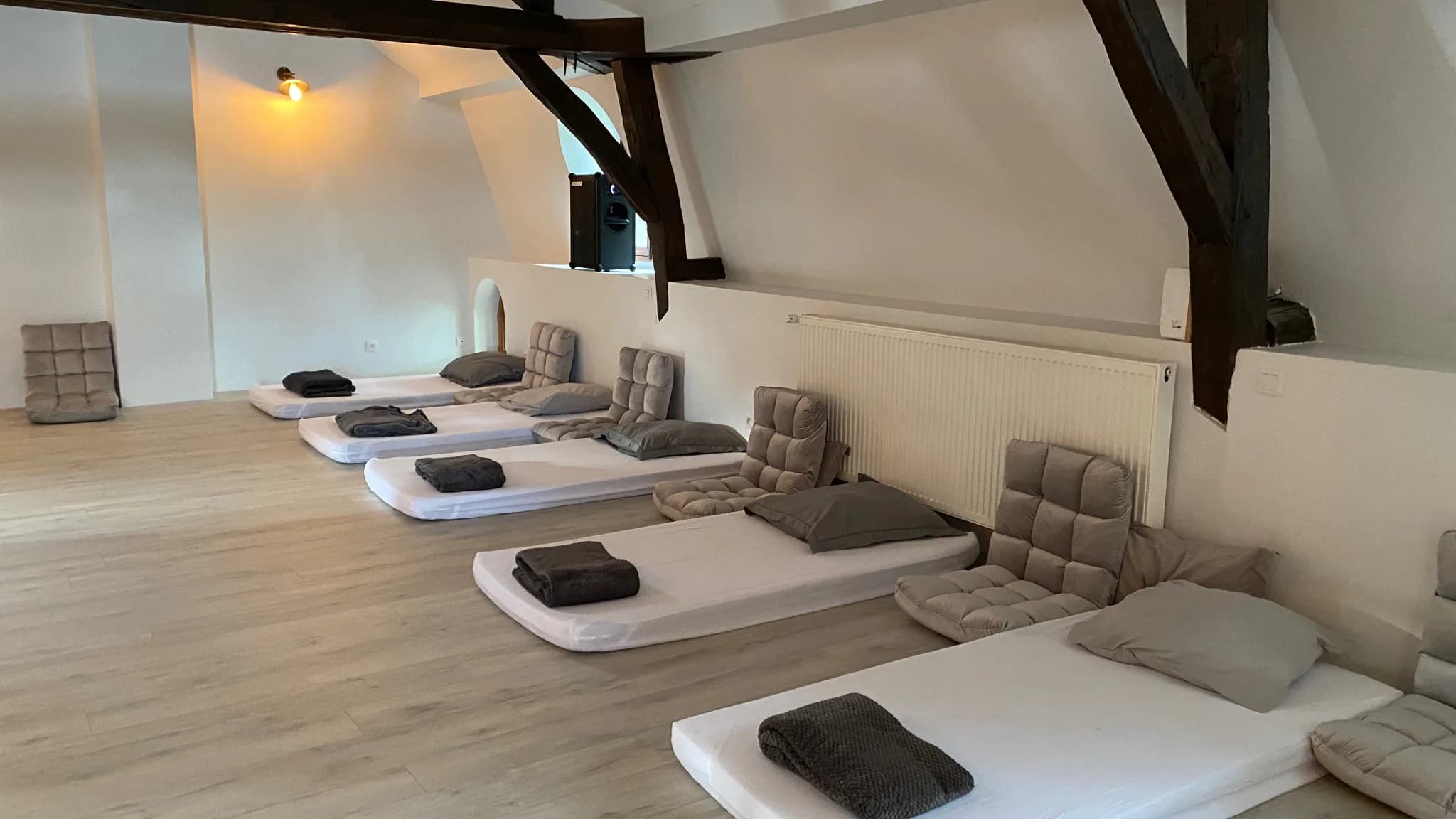 La salle de pratique préparée pour un séminaire : matelas alignés au sol, plaids pliés et coussins de sol, sous la charpente du Moulin d’en Bas.